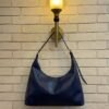 Navy blue hobo shoulder bag with a tonal strap against a brick wall