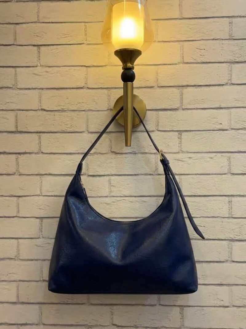 Navy blue hobo shoulder bag with a tonal strap against a brick wall