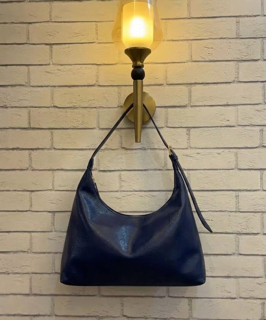 Navy blue hobo shoulder bag with a tonal strap against a brick wall