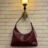 Burgundy hobo shoulder bag with a tonal strap against a brick wall
