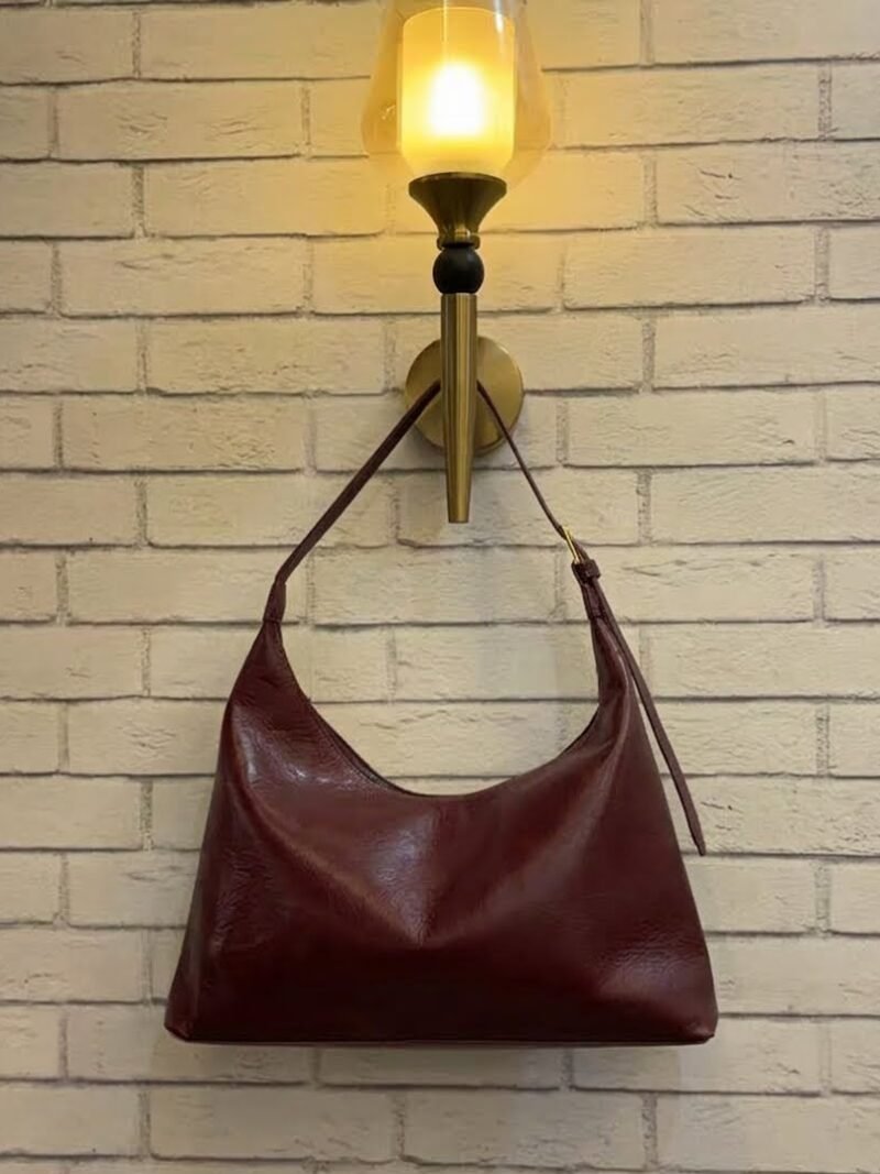 Burgundy hobo shoulder bag with a tonal strap against a brick wall