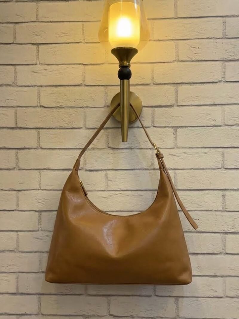 Caramel Tan hobo shoulder bag with a tonal strap against a brick wall